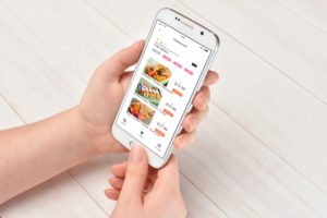 Food Apps und Vitamin B12. Das Foto zeigt ein Mädchen, das an einem Tisch sitzt und mit Hilfe einer App etwas zu Essen bestellt.