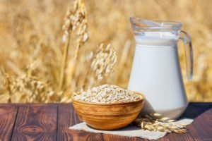 Haferdrink in der Karaffe neben einer Schüssel Hafer. Enthalten Pflanzendrinks Vitamin B12?